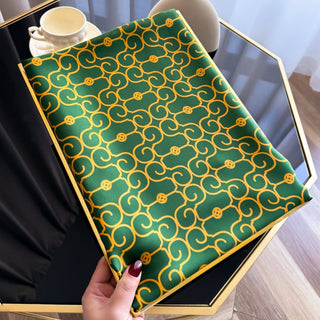 Green fabric with gold pattern held by a hand, placed on a black surface.