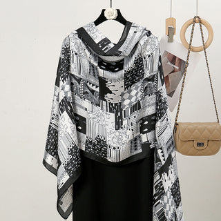 Black and white patterned scarf draped over a black dress on a hanger with a beige handbag in the background.