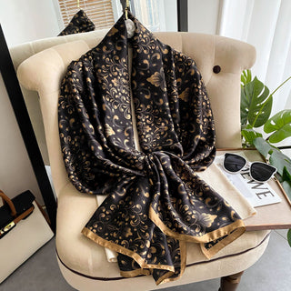Black and gold patterned scarf draped over a beige chair with a plant and magazine in the background.