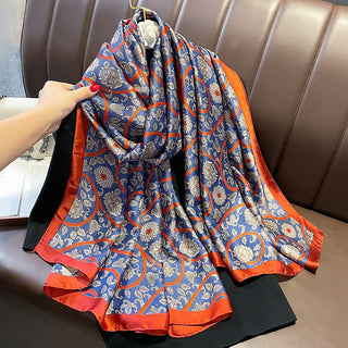 A vintage royal blue floral design women's satin silk scarf held up against a light background, displaying its geometric pattern and royal blue color with a border in a different design.
