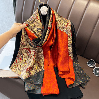 A multicolored satin silk scarf with a geometric pattern, draped over a chair, featuring shades of gold, red, and black.